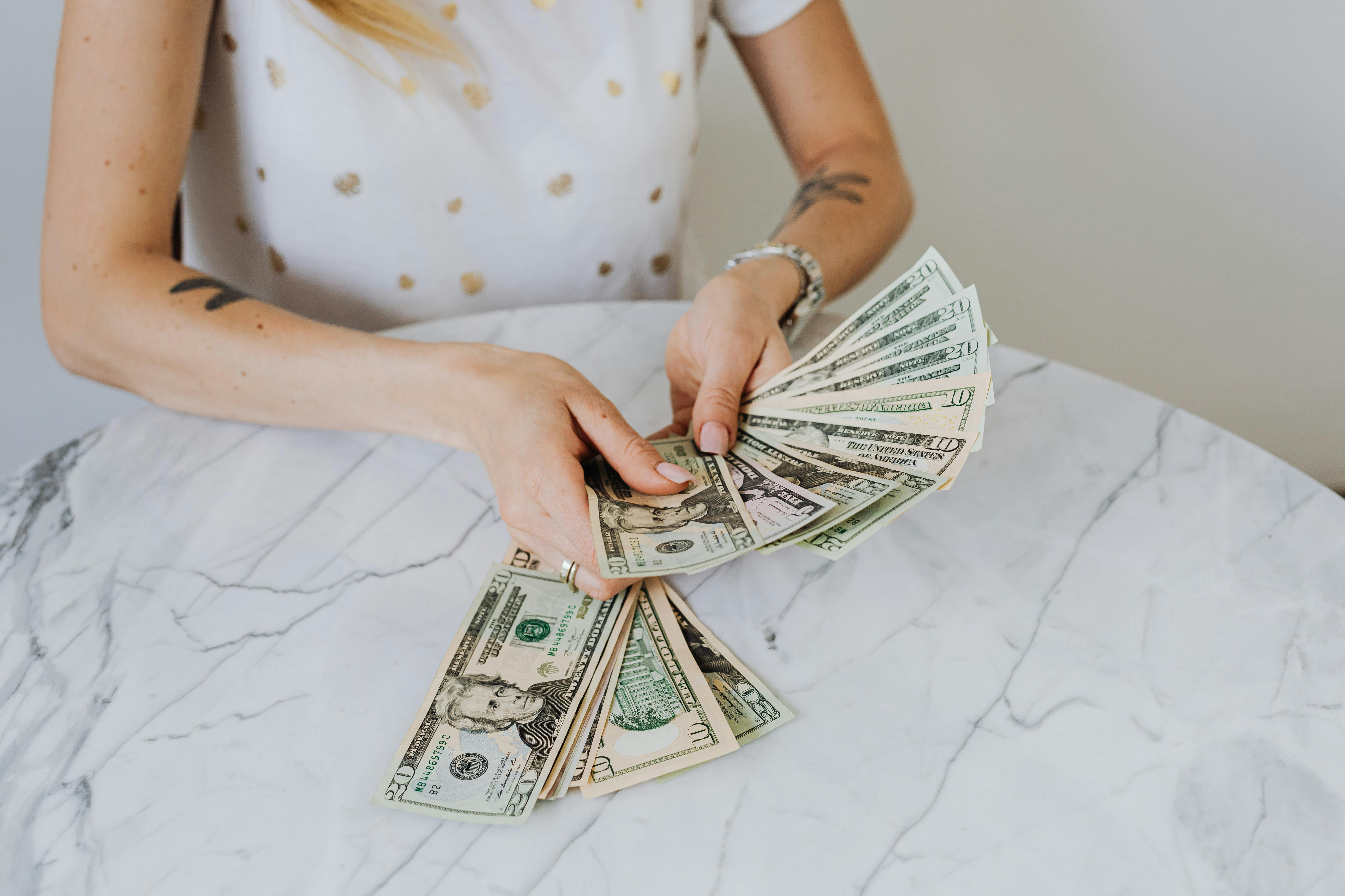 A woman holds a wad of money on a table.